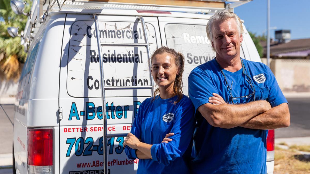 Plumbing apprentice stands with trade professional in front of van.