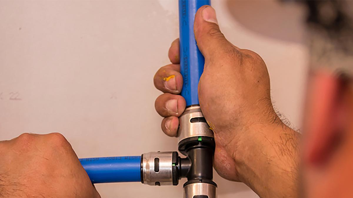 Close-up of of hands holding blue PEX pipe connected to an EvoPEX fitting.