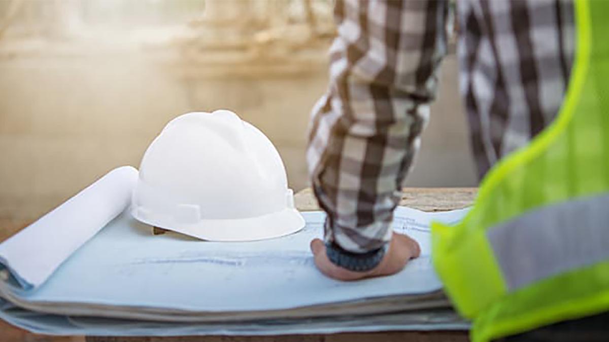 Close-up of a person standing in front of blueprints and a hard hat.