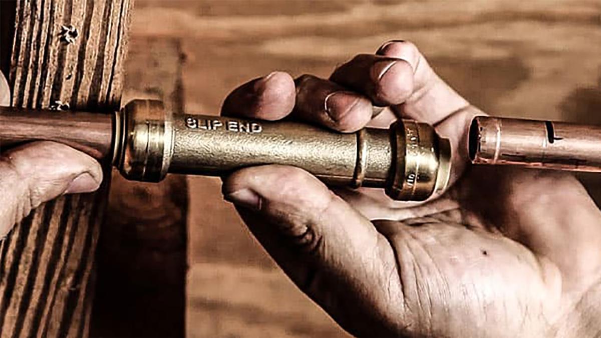 Hands connecting two copper pipes with a slip end fitting.