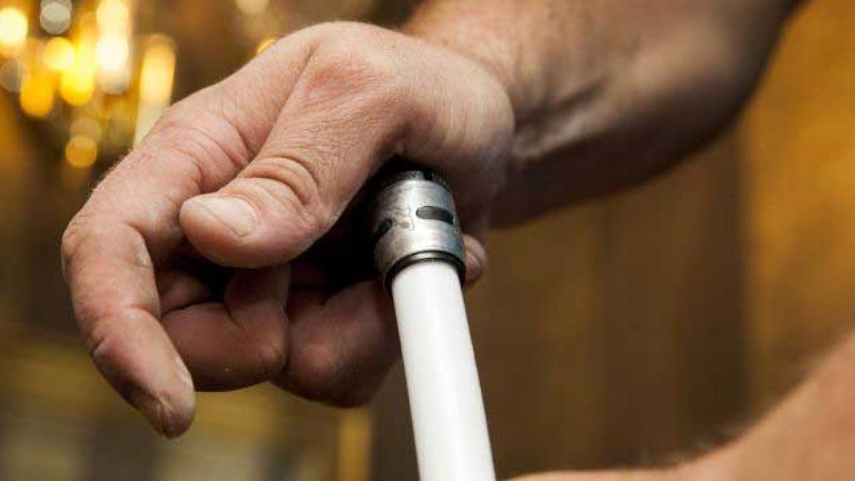 Close-up of hands connecting an EvoPEX fitting with a white PEX pipe.