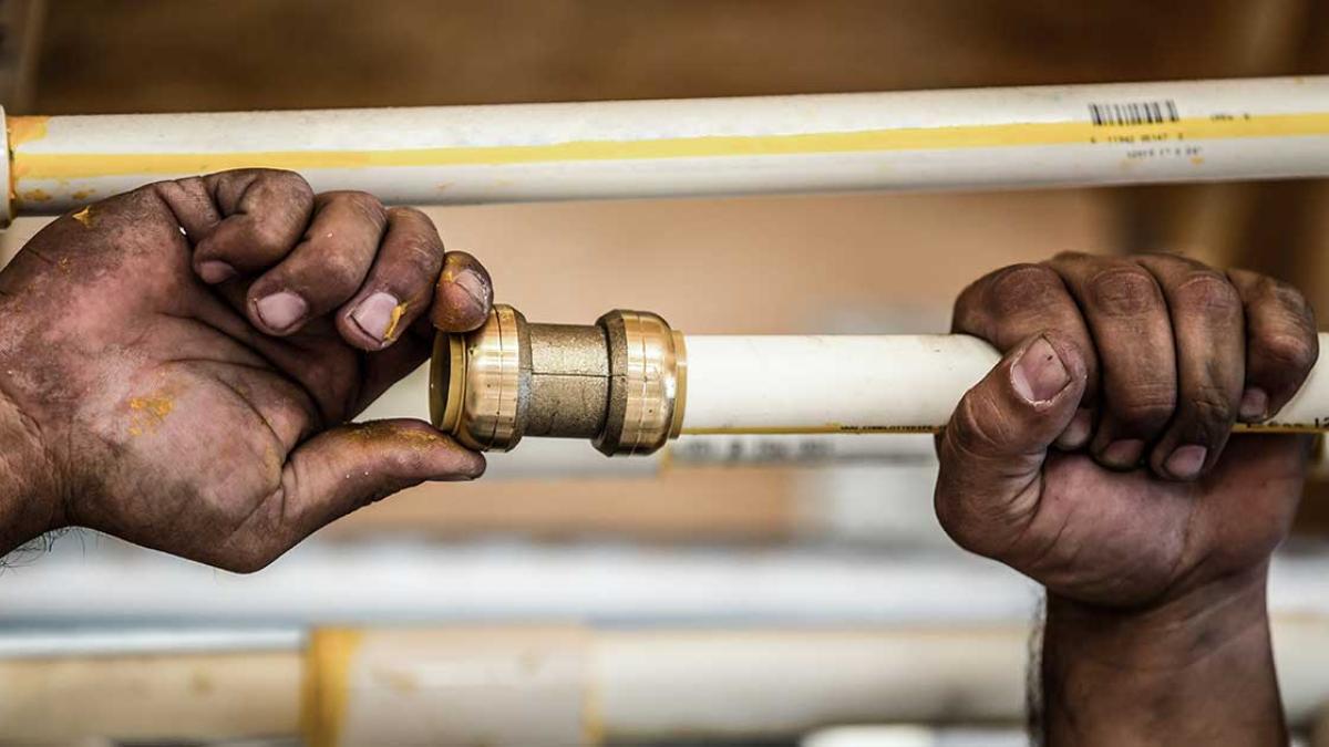 Close-up of dirty hands connecting a push-to-connect fitting to white pipe.