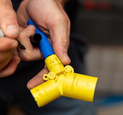 Installer marking insertion depth on blue PEX pipe using a SharkBite depth gauge and deburring tool.