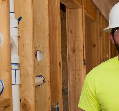A plumber walking through a new build carrying red SharkBite PEX pipe