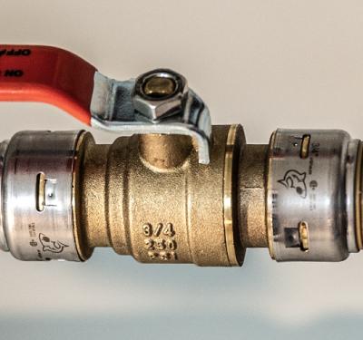 SharkBite brass push-to-connect ball valve installed between PVC and PEX pipe, featuring a tool-free connection for pressure regulation and flow control applications.
