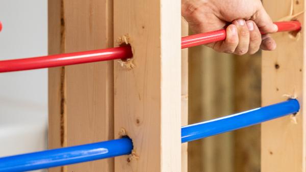 Red and blue PEX pipe running through wooden wall framing during installation.