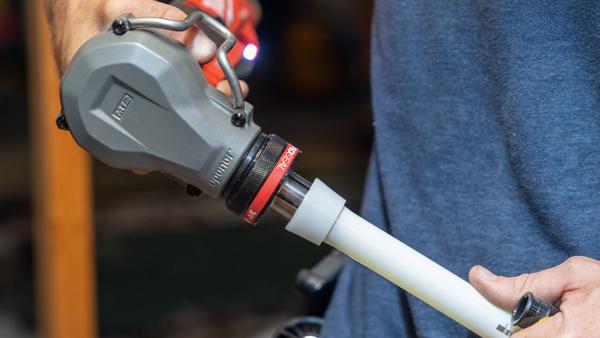 Person using a PEX expansion tool on white PEX pipe.