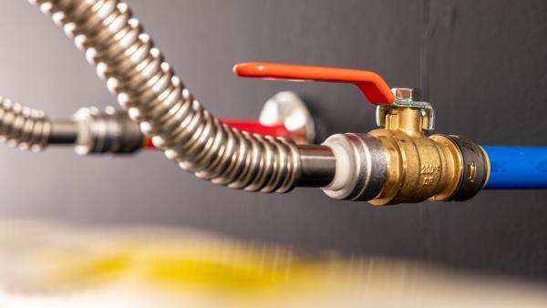 Close-up of a brass shutoff valve installed between a stainless steel water heater connector and blue PEX tubing