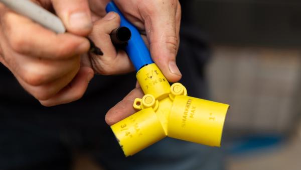 Installer marking insertion depth on blue PEX pipe using a SharkBite depth gauge and deburring tool.