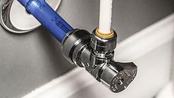 Close-up of a push-to-connect shutoff valve connecting blue and white PEX pipes to a water supply
