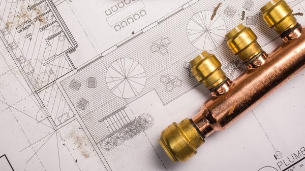 SharkBite brass push-to-connect plumbing manifold system shown on home blueprint design, featuring multiple color-coded outlet branches for individual room water control and simplified whole-house distribution configuration