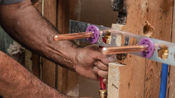 SharkBite brass push-to-connect plumbing manifold system shown on home blueprint dplumber installing SharkBite brass push-to-connect stub-out elbow during rough-in phase, allowing for pressure testing before fixture installation with secure, tool-free connection for exposed copper or PEX pipe