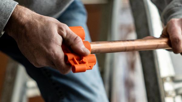 plumber using SharkBite pipe cutting and preparation tool on copper pipe for push-to-connect fitting installation, demonstrating essential accessory for clean, precise cuts ensuring leak-free connections