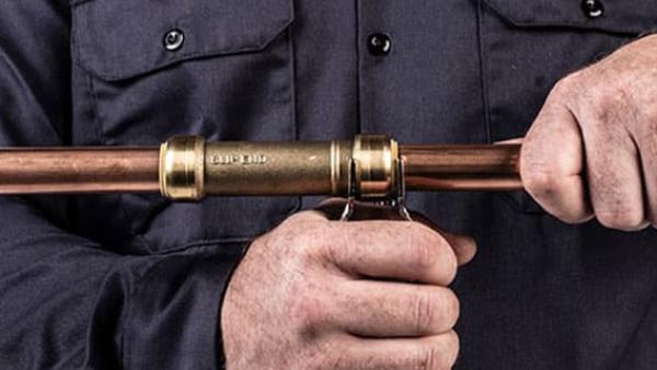 A close-up image of a person installing a brass push-to-connect plumbing fitting onto a copper pipe