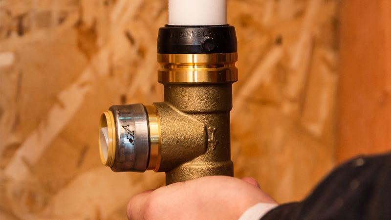 A contractor installs a SharkBite large diameter fitting onto white PEX pipe. 