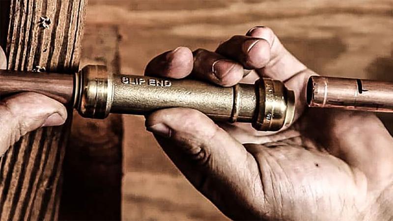 Hands connecting two copper pipes with a slip end fitting.