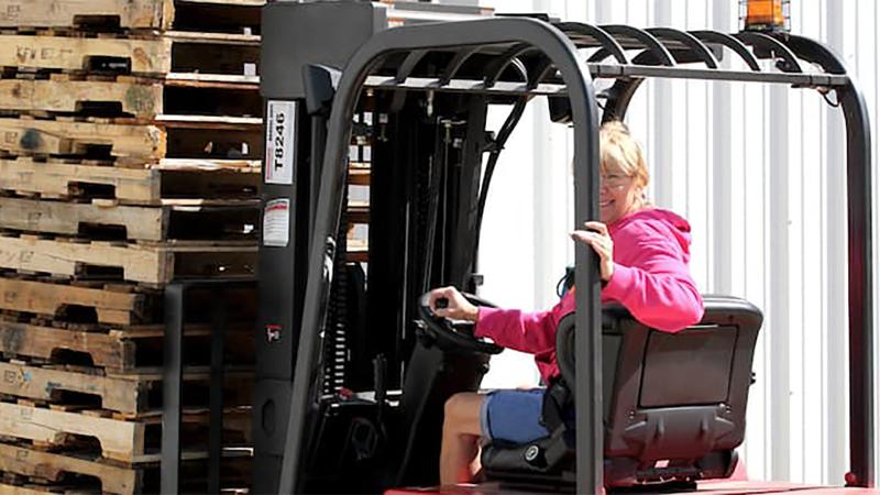 Image of a woman on a forklift carrying wooden pallets. 