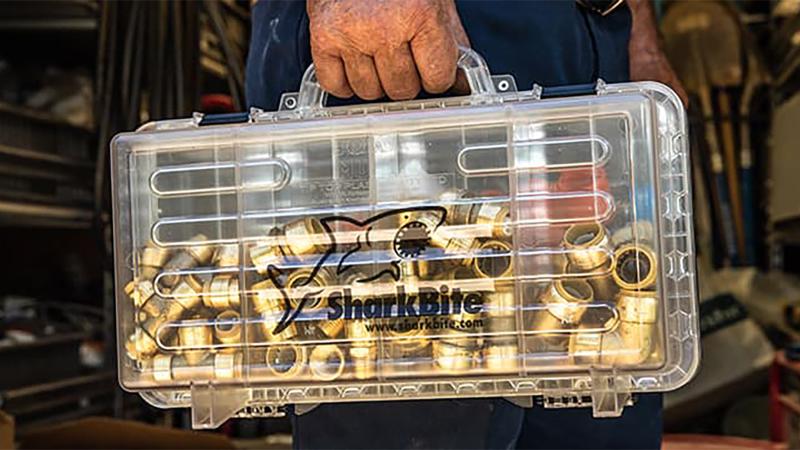 Close up  of hands holding a clear SharkBite toolbox filled with SharkBite fittings.