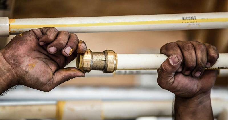Close-up of dirty hands connecting a push-to-connect fitting to white pipe.